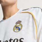 Close-up van het clublogo en gouden details op het witte Real Madrid thuisshirt uit het seizoen 2025-26