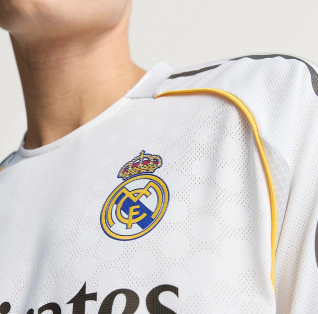 Close-up van het clublogo en gouden details op het witte Real Madrid thuisshirt uit het seizoen 2025-26